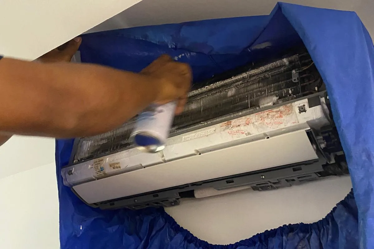 Technician spraying chemical cleaner into the opened coil of a wall-mounted aircon unit in Singapore