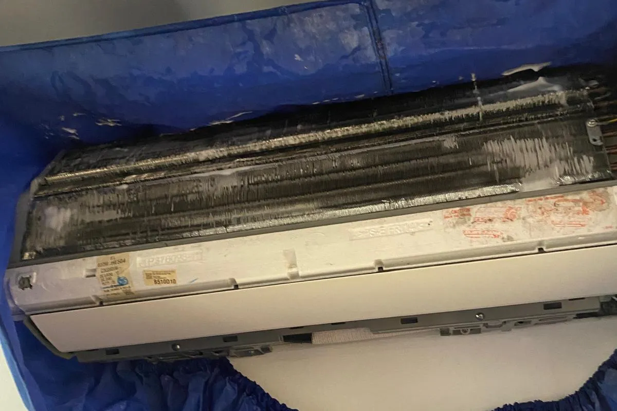Blackened aircon evaporator coil exposed above a blue chemical overhaul service bag