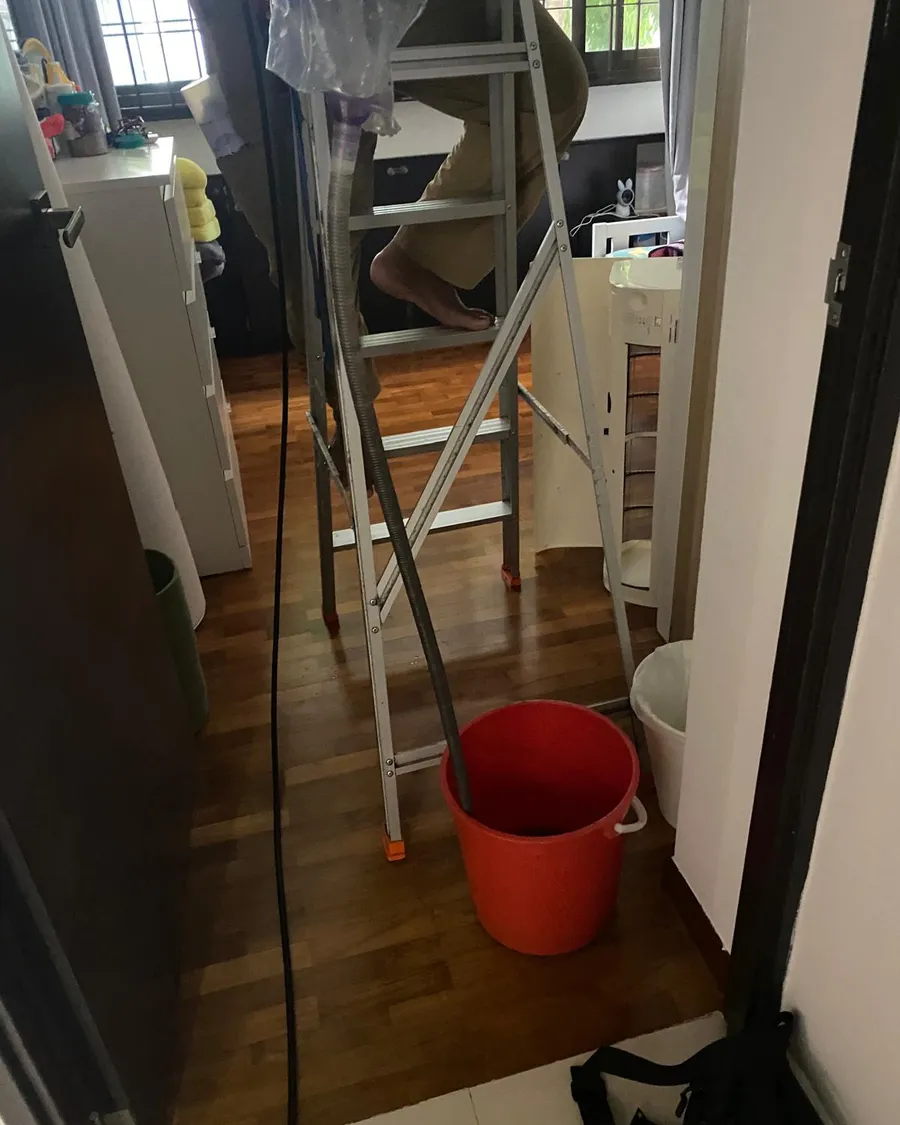 Ladder and collection bucket set up under an aircon unit being serviced in a Singapore flat