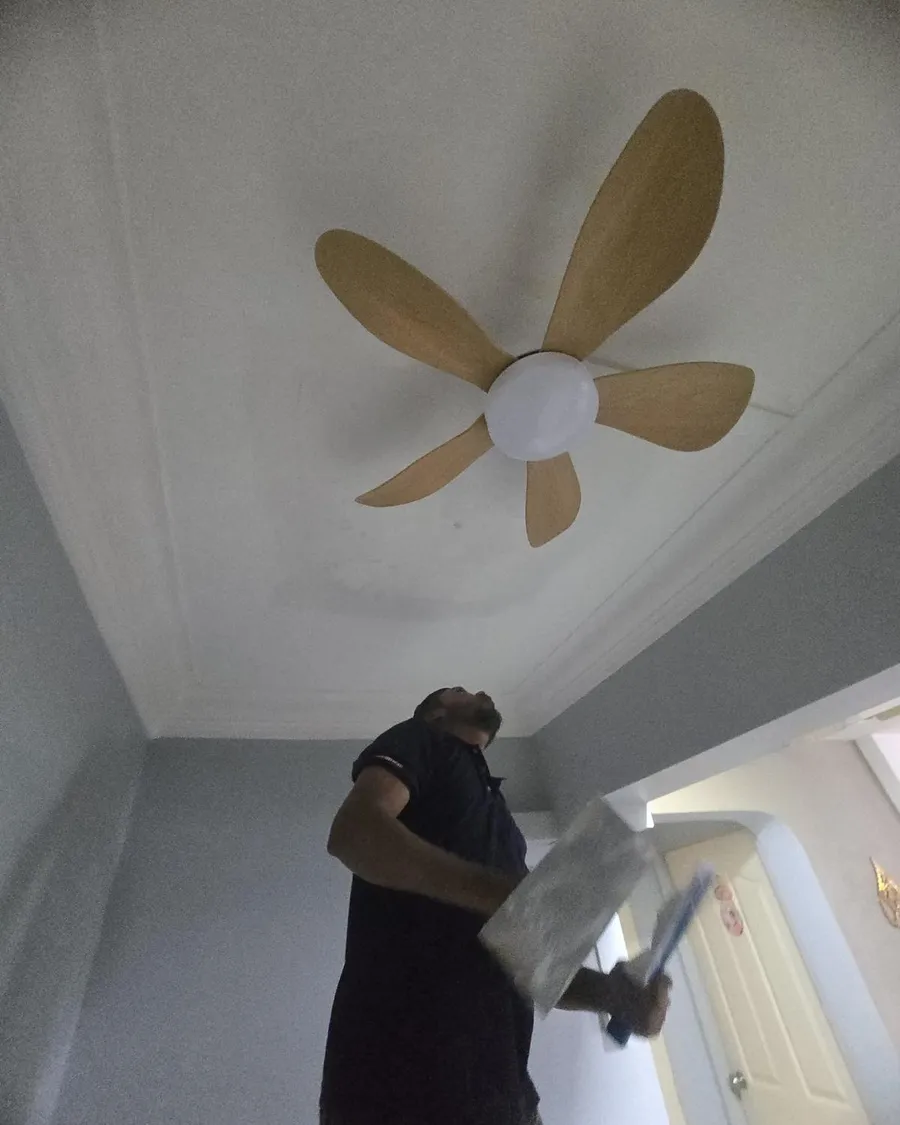 Technician unwrapping a ceiling fan blade below an installed five-blade fan in a Singapore flat
