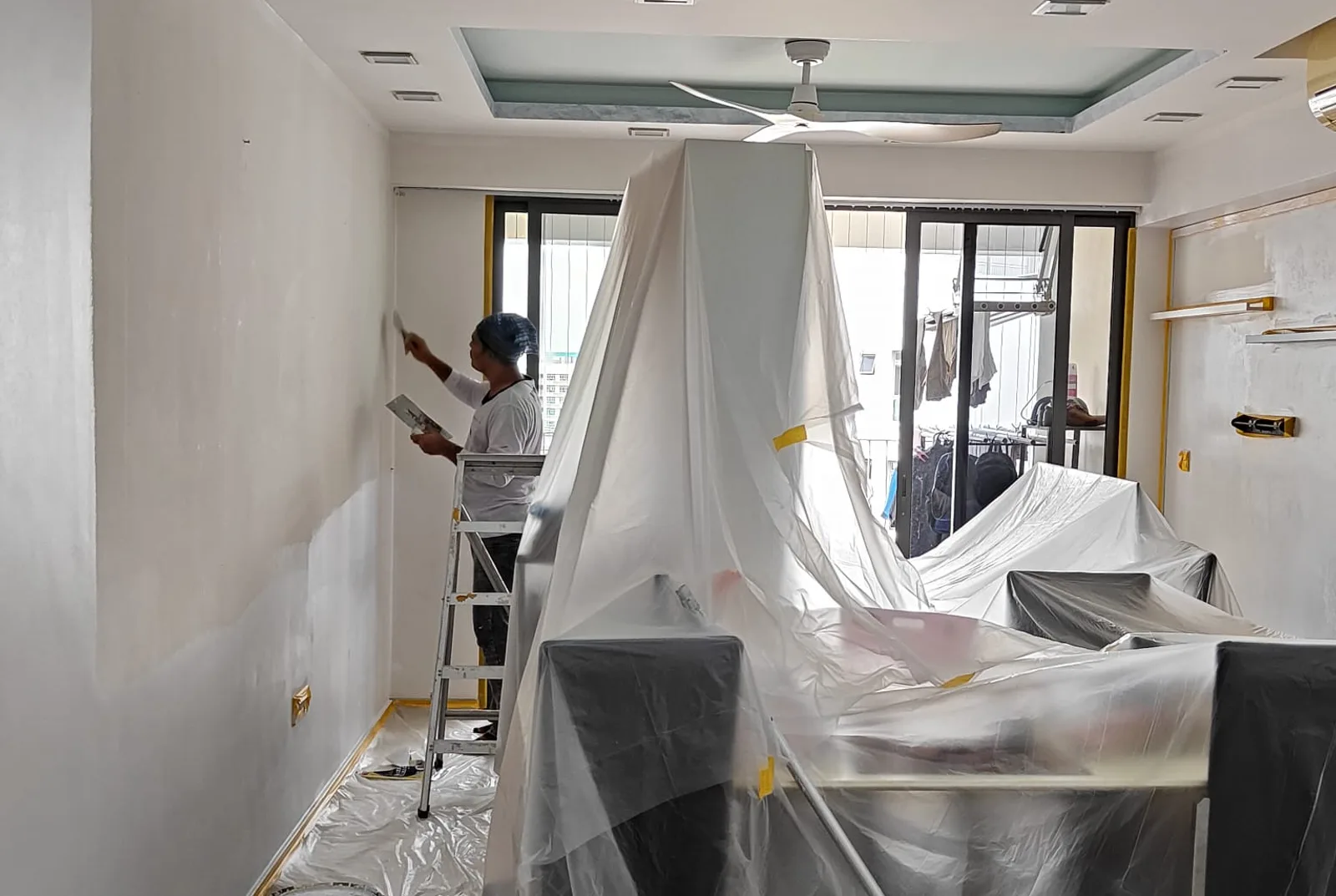 Painter on a ladder painting a condo living room in Singapore with the furniture sheeted