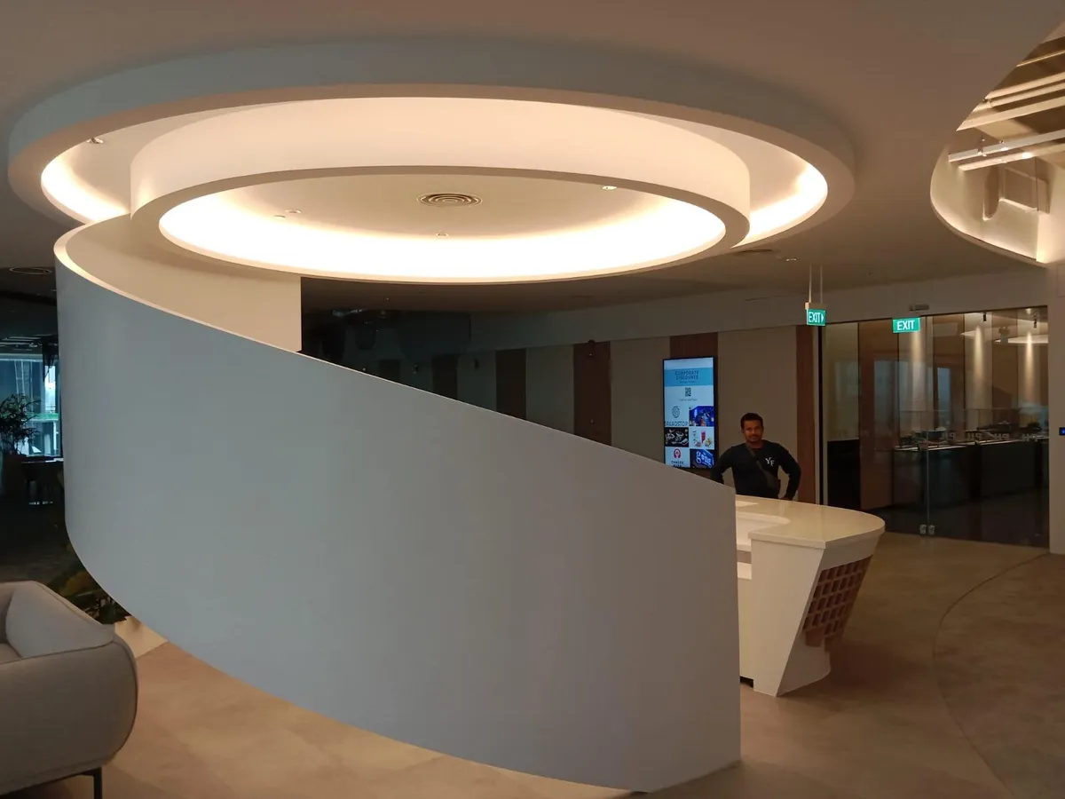 Curved reception counter below a circular cove-lit false ceiling in a Singapore office
