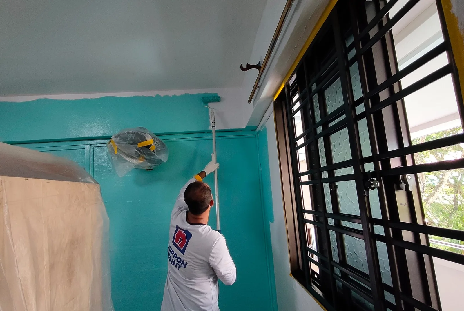 Painter cutting in the ceiling line above a teal feature wall in a Singapore HDB flat