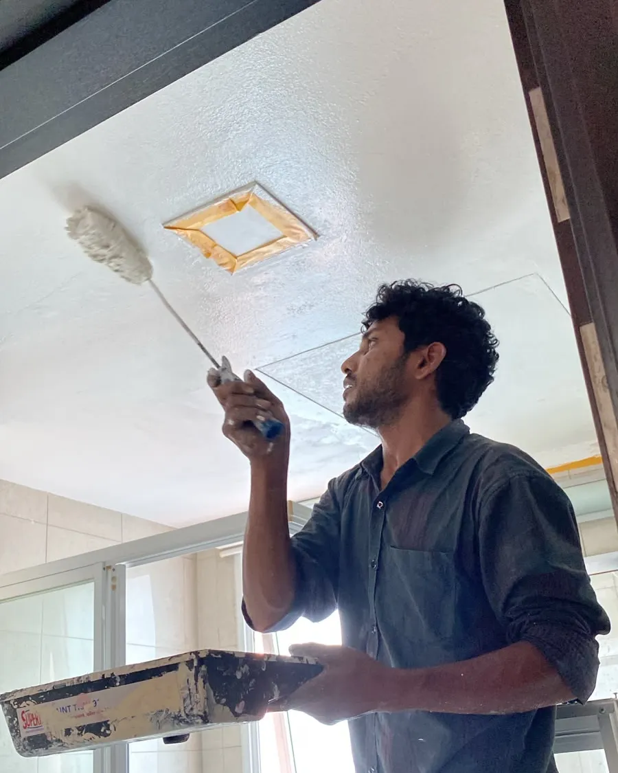 Painter rolling a toilet ceiling in Singapore with the extractor vent masked off